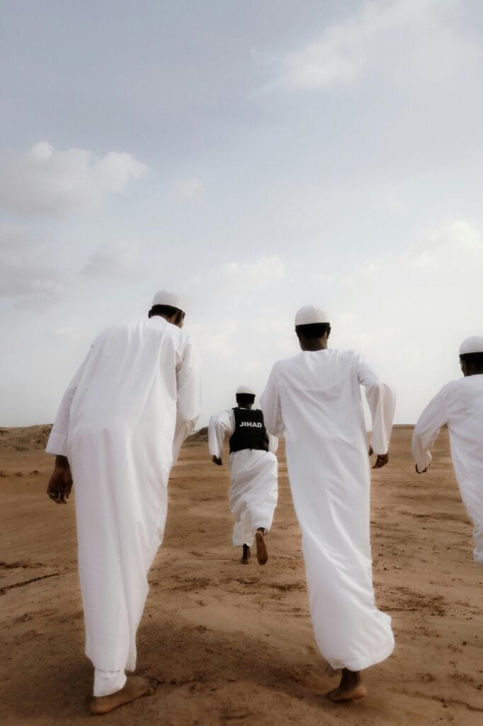 Group of men in white robes walking across a sandy desert in Nigeria.