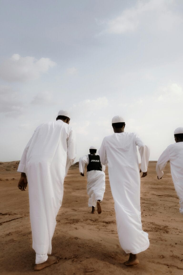 Group of men in white robes walking across a sandy desert in Nigeria.