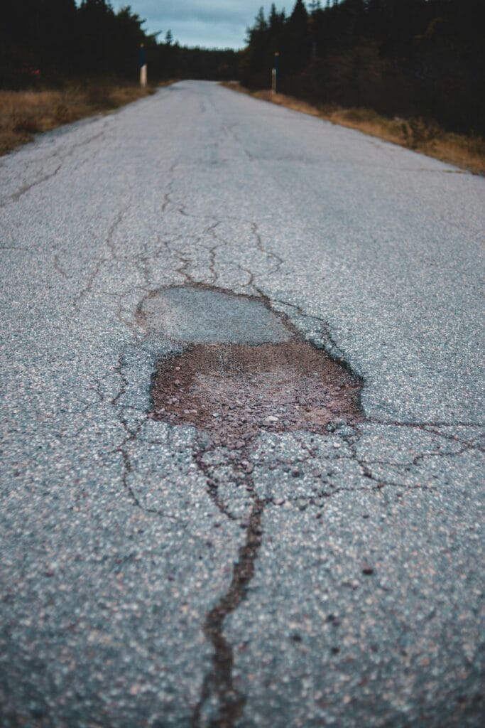 From above of cracks and hole on empty narrow aged asphalt road going along lush green trees growing in forest