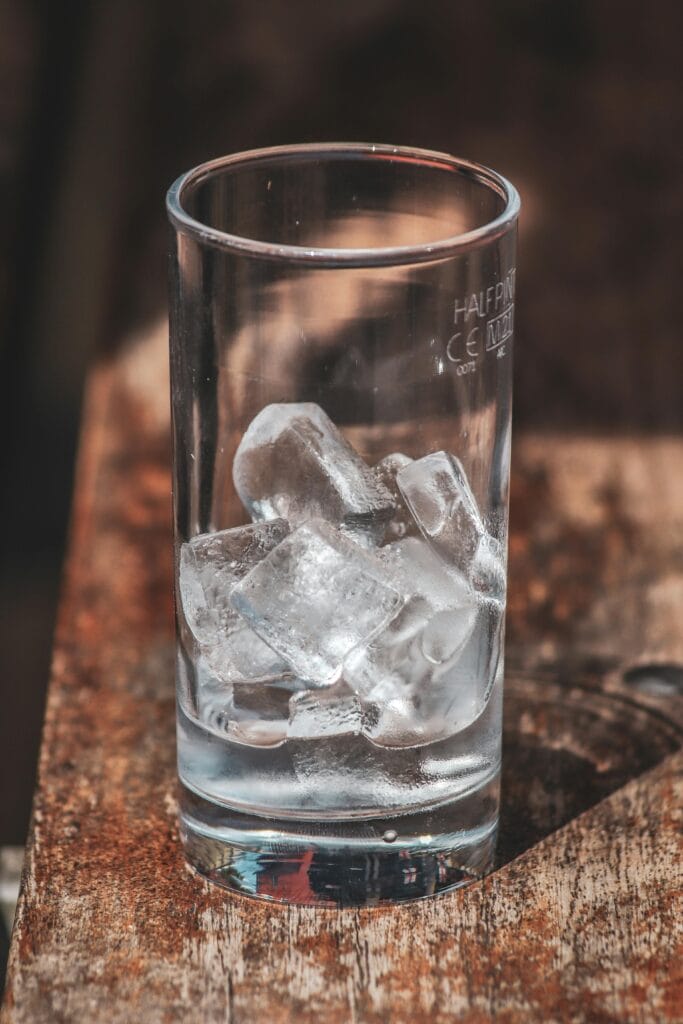 A close-up view of clear ice cubes in a glass on a rustic wooden surface, showcasing texture and simplicity.