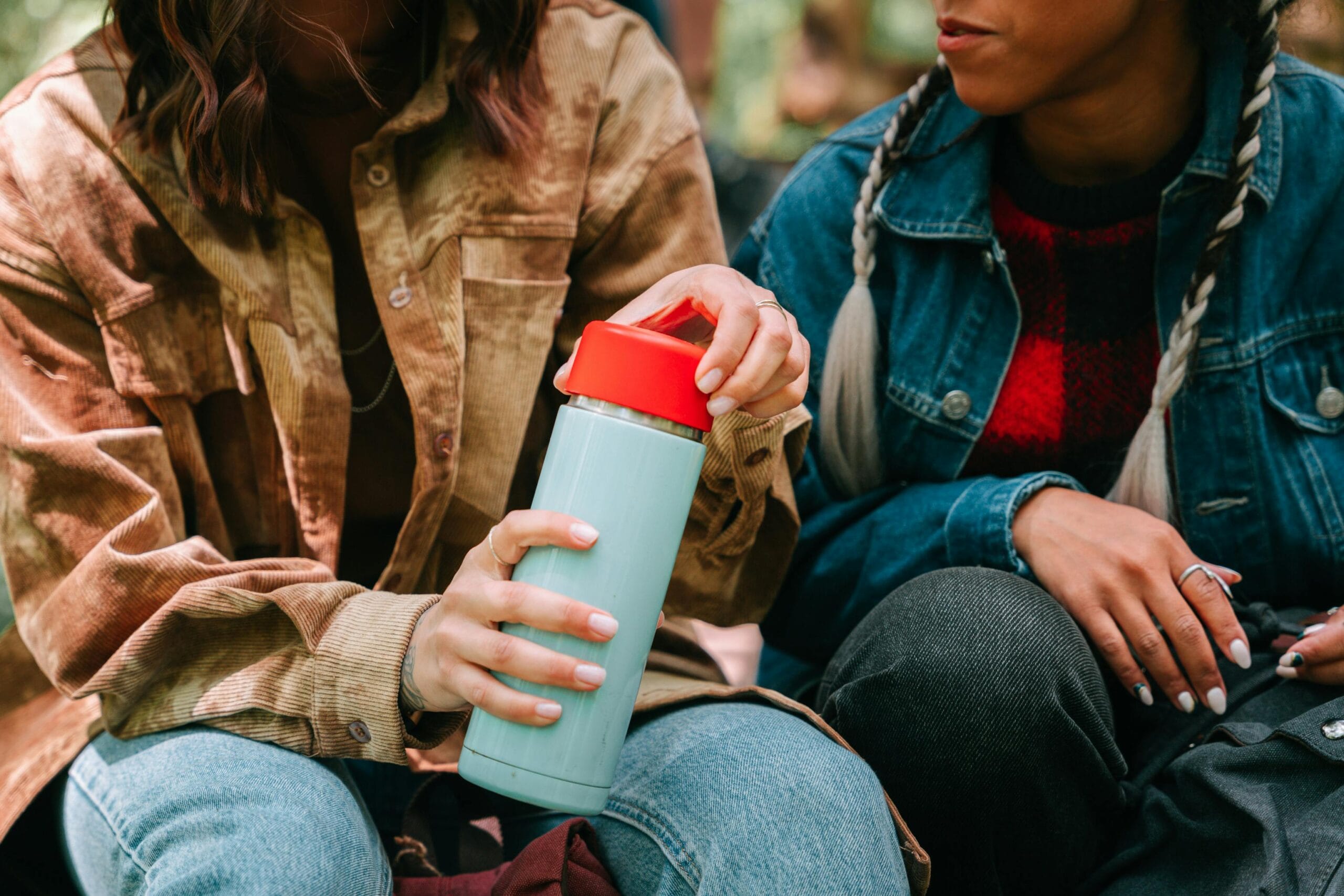 Two friends enjoying outdoor time with a reusable water bottle, showcasing eco-friendly lifestyle.